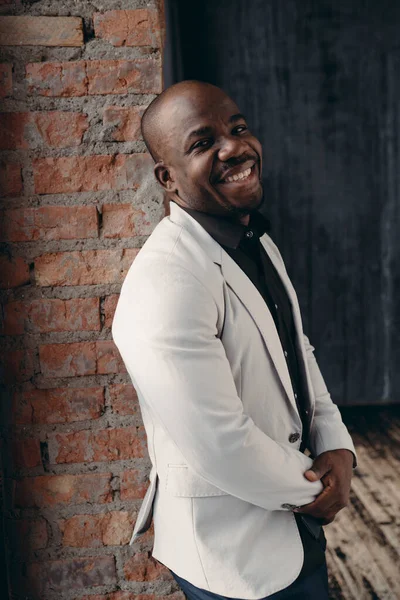 Africano americano homem posando na câmera, sorrindo, encostado contra a parede no loft studio.Style e conceito de negócios — Fotografia de Stock