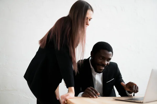 Бизнесмен в костюме сидит и смотрит в компьютер, а рядом с ним стоит девушка с длинными волосами. — стоковое фото