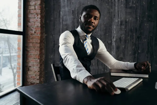 O homem de negócios elegante em uma camisa senta-se em uma cadeira em uma mesa em um escritório que faz o trabalho de computador — Fotografia de Stock