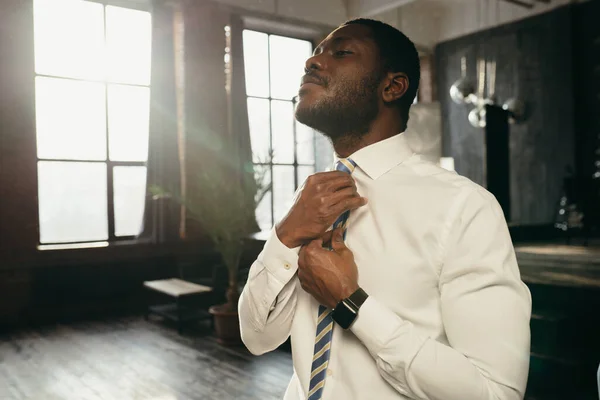 Bonito empresário de camisa levantou a cabeça e endireita sua gravata em uma casa ensolarada — Fotografia de Stock