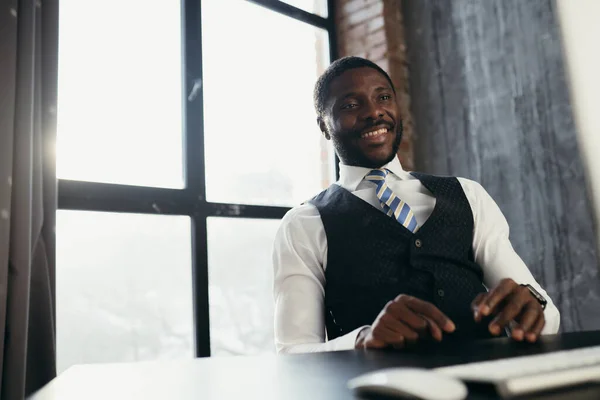 Africano homem americano trabalhando com gadgets modernos contra o pano de fundo de uma grande janela — Fotografia de Stock