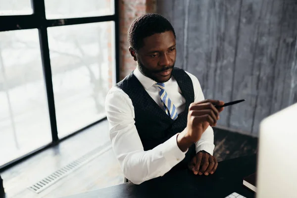 Africano homem americano trabalhando com gadgets modernos contra o pano de fundo de uma grande janela — Fotografia de Stock