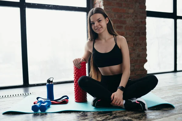 Vacker flicka i svart topp förbereder sig för övningar i gymmet medan du sitter på en sportmatta — Stockfoto