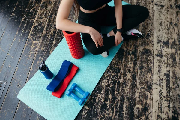 Foto ovanifrån. Sportutrustning av gummiband och hantlar bredvid vilka flickan sitter — Stockfoto