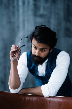 Sandalyeye yaslanmış mavi yelekli, beyaz gömlekli Hintli adam.