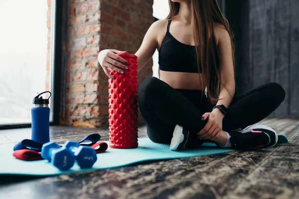 Trainer într-un top negru și jambiere stă pe un covor în sala de gimnastică cu termos și benzi elastice sportive — Fotografie, imagine de stoc