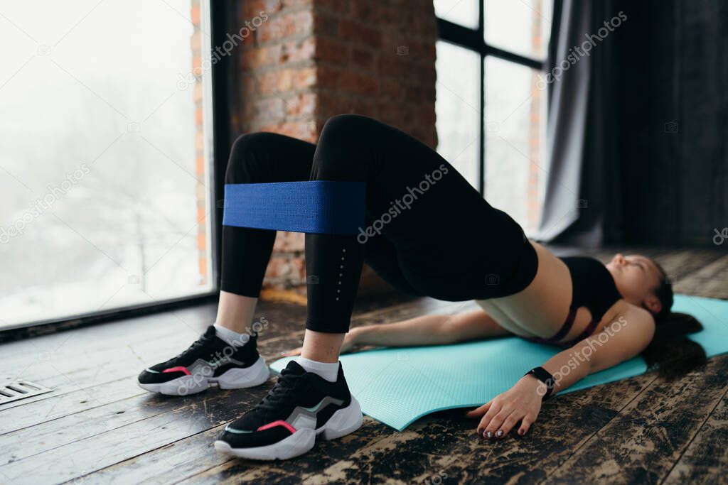 A girl lying on the mat does an exercise with raising the torso above the floor using sports elastic bands