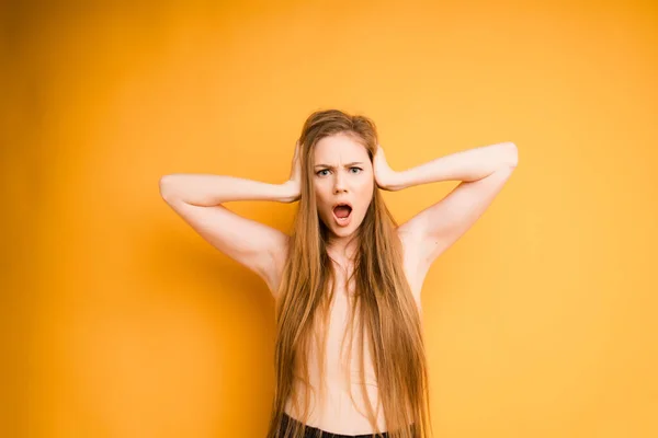 Atraktivní běloška s dlouhými vlasy drží hlavu rukama a křičí na oranžovém pozadí. Emocionální žena — Stock fotografie