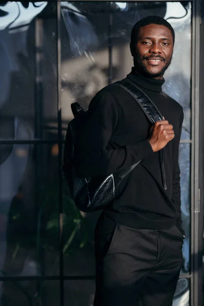 Estudante de gola alta preta com uma mochila nas costas sorrindo para a câmera — Fotografia de Stock