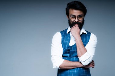 Mavi yelekli, gözlüklü bir Hindu düşünceli bir bakışla başka yere bakar.