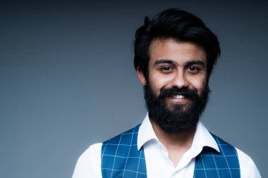 Beyaz gömlekli, siyah sakallı, kameraya gülümseyen yakışıklı Hindu adam.