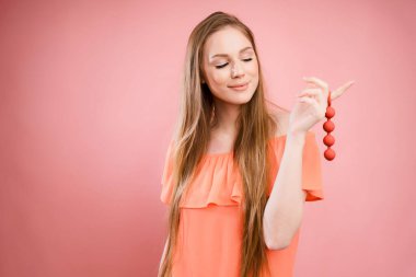 A woman holds Kegel balls on her finger to strengthen the muscles of the vagina. Portrait with a sex toy for pleasure on a pink background
