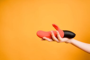 Female hand with a dildo for masturbation and orgasm in women. Clitoris massager, toys for adults on orange background, space for text