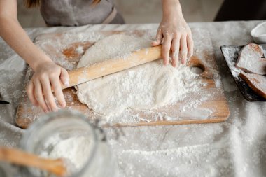Kadın eli un içinde, masada merdaneyle hamuru yuvarlıyor. Yemek pişirme konsepti