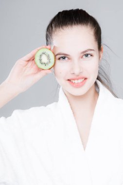 Çekici bir kızın portresi açık arka planda yüzüne bir dilim kivi yapıştırıyor.