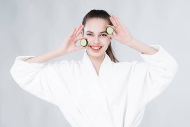 Temiz yüzlü bir kadın yüzüne sürerek salatalık maskesi yapar. Evde bakım