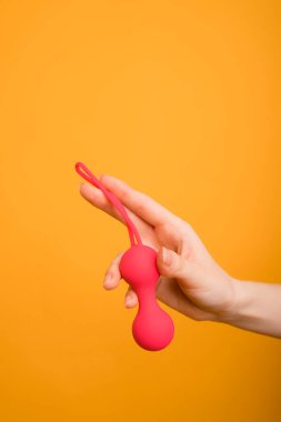 Kadın eli kırmızı Kegel toplarını tutuyor ve turuncu arka planda zafer işareti gösteriyor. Bir kadının elinde vajinal toplar. - Evet. Mesaj için yer. Seks dükkanı konsepti