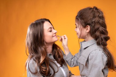 Beautiful woman sits with closed eyes while a little girl does her makeup while holding a brush in her hands