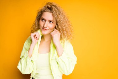 A charming young girl stands on a bright background in a green jacket and holds a collar with her hands