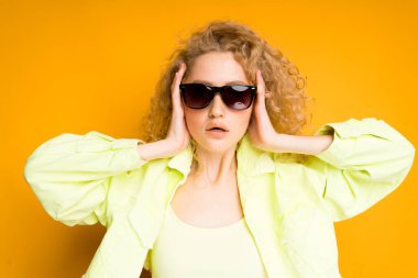 Yeşil ceketli çekici bir genç kız, gözlüklü, elleriyle başını kapatıyor.