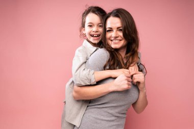 Gömlekli çekici bir kız, elbiseli ve dalgalı saçlı gülümseyen bir anneye sarılıyor. Aile kucaklaşması.