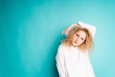 Sarı kıvırcık saçlı tatlı bir kız bir elini başının arkasına atar ve kameraya bakar.