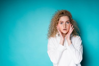 Beyaz gömlekli hoş bir kadın avuçlarıyla yüzüne dokunuyor, ağzını açıyor.