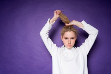 Kıvırcık sarı saçlarını tutup kaldırarak at kuyruğu yapan çekici, ciddi bir kız.