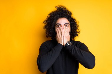 Saçları afro saçlı genç Mısırlı. Avuç içleri avuçlarıyla kaplı. Sarı arka planda dururken sadece gözleri görünüyor.