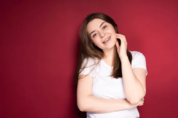 Mulher bonita em aparelho sorrindo alegremente inclinando a cabeça para um lado enquanto estava em pé no fundo vermelho — Fotografia de Stock