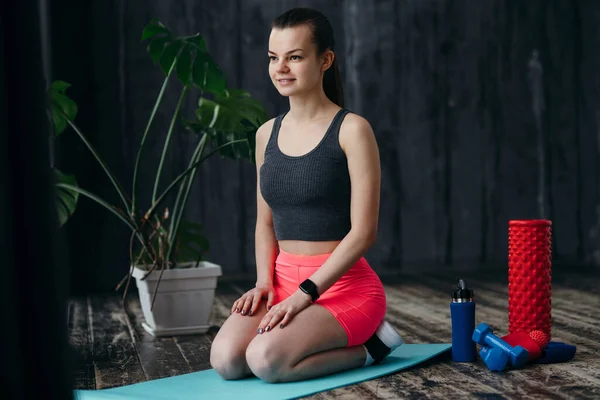 Zâmbind antrenor de fitness care efectuează yoga în timp ce stă pe mat în sala de sport cu fascie și sticlă de apă — Fotografie, imagine de stoc