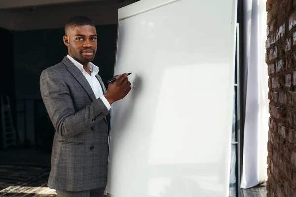Africano americano empresário negociação fazendo desenho com marcador no quadro branco olhando para a câmera — Fotografia de Stock