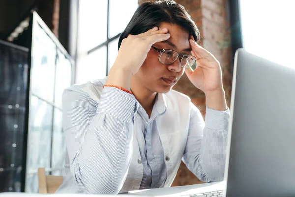 Азиатский бизнесмен в очках работает за компьютером и трогает виски из-за головной боли. — стоковое фото