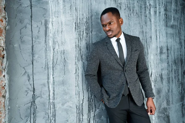 Serious stylish black businessman in formal suit leans on the wall and looks to the side