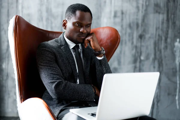 Cansado empresário afro-americano trabalhando no laptop e pensando, apoiando-se no punho — Fotografia de Stock