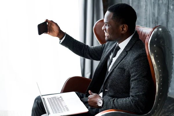 Feliz homem americano africano trabalhando no laptop e tirando selfie no telefone sorrindo — Fotografia de Stock