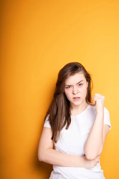 Uma menina com cabelos longos fica contra um fundo amarelo e está com raiva por causa da dor na cabeça e dentes — Fotografia de Stock