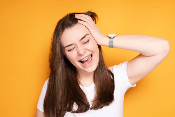 Cheerful girl with braces laughs opening her mouth and tilts her head to the side, touching her hand to it — Stock Photo, Image