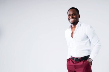 Tişörtlü, esmer, neşeli bir adam. Bir eli pantolonunun cebinde kameraya bakıyor ve gülümsüyor.