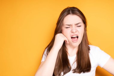 Genç bir kız, gözlerini kapatıp eliyle çenesine dokunarak diş tellerinin takılması nedeniyle baş ve diş ağrısından muzdarip.