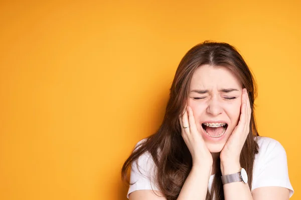 Dívka s rovnátky ječí bolestí hlavy a bolestí zubů a dává si ruce na obličej — Stock fotografie