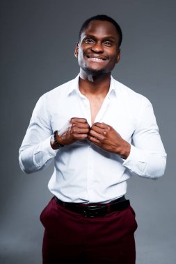 Mutlu Afro-Amerikalı adam işe giderken gömleğinin düğmelerini ilikleyecek. Gülümseyecek ve gri arka planda duracak.