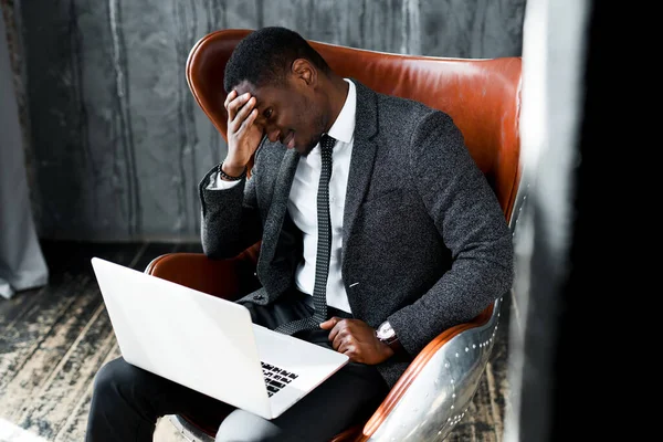 Unavený africký americký podnikatel v obleku pracuje na notebooku, zatímco sedí v křesle — Stock fotografie