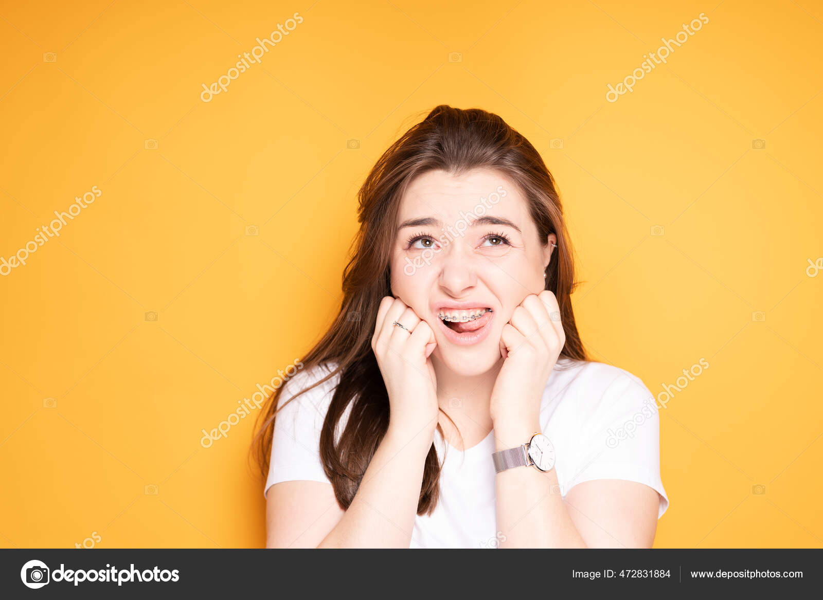 Beautiful young girl with braces puts her hands to the jaw due to tooth