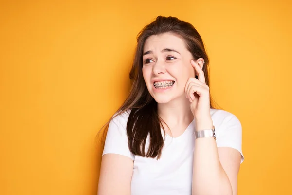 Menina atraente com aparelho grimaces de dor nos dentes, olhando para longe. Conceito de sorriso saudável — Fotografia de Stock