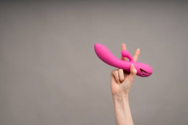 A womans hand holds a pink dildo or massager for sex and shows the Victoria gesture with her fingers.