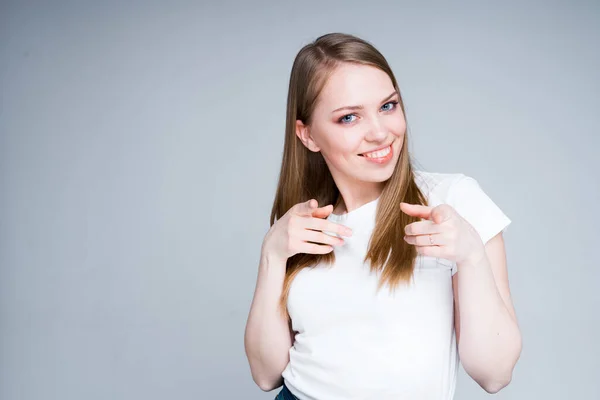 Χαριτωμένο νεαρό κορίτσι σε ένα λευκό t-shirt δείχνει τα δάχτυλα στην κάμερα αναζητούν ενδιαφέρον — Φωτογραφία Αρχείου