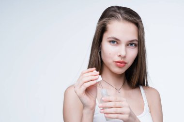 Çekici bir kız elinde serum olan bir damlacığı tutuyor ve kameraya bakıyor. Beyaz arkaplanda izole