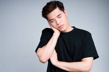 Siyah tişörtlü genç Asyalı adam koluna yaslandı ve gözlerini kapattı.