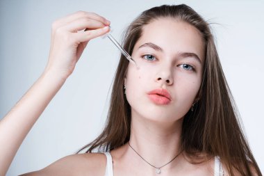 Temiz ciltli güzel bir kız yüzüne pipetle serum sürüyor. Cilt bakımı kavramı